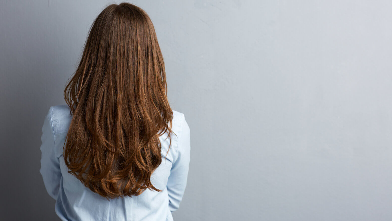 business-woman-standing-back-against-gray-wall-long-hair