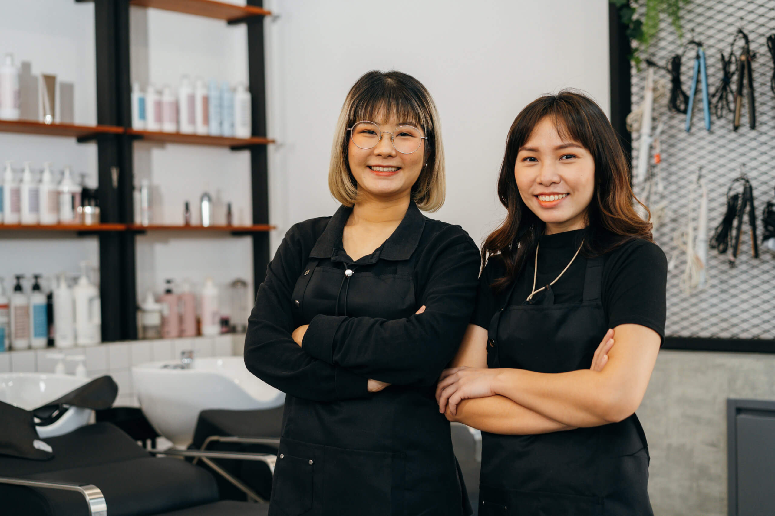 Two hairstylist women wearing black, cross arm and smiling