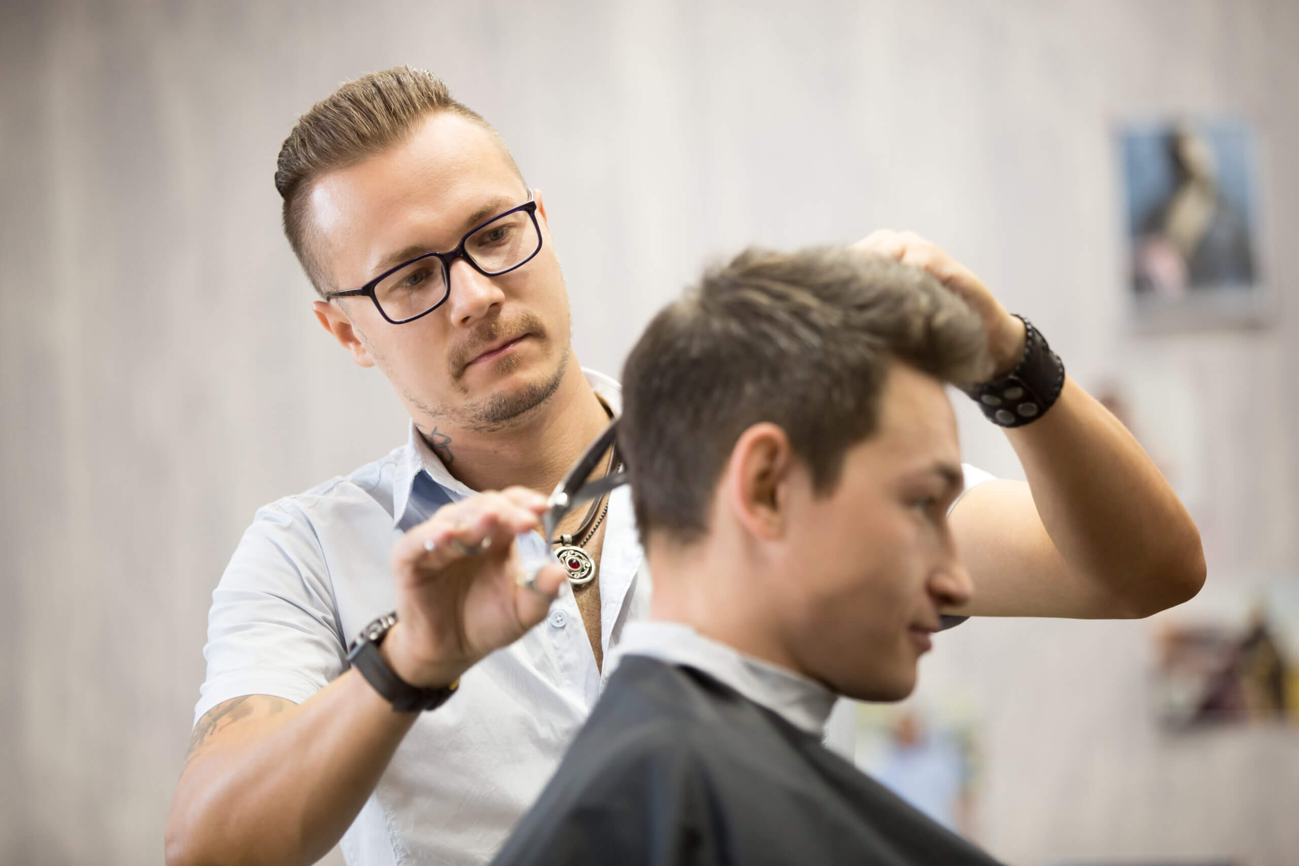 Male hairdresser making haircut working process modern barbershop serving client using metal scissors side view attractive