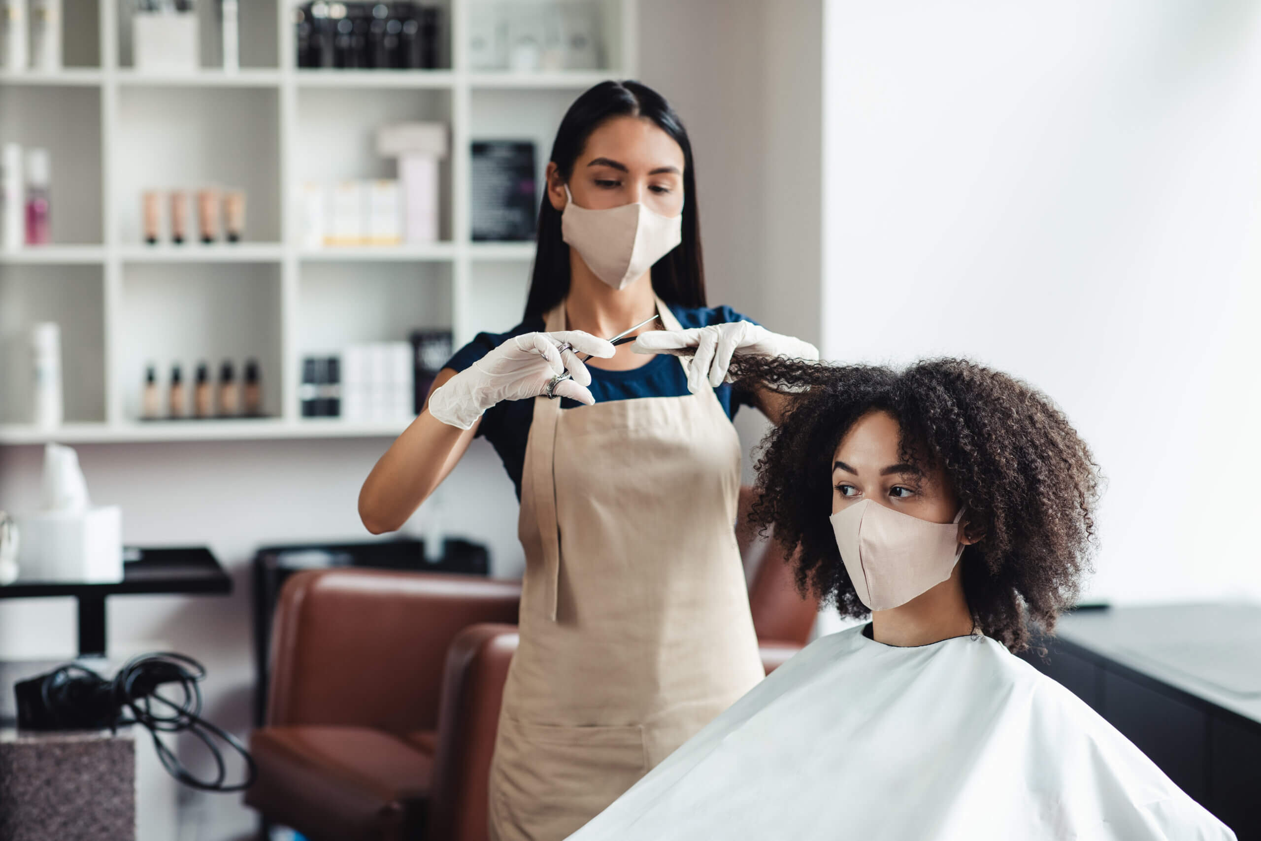 Beauty treatment after isolation. Young black girl in protective mask getting haircut at salon, free space