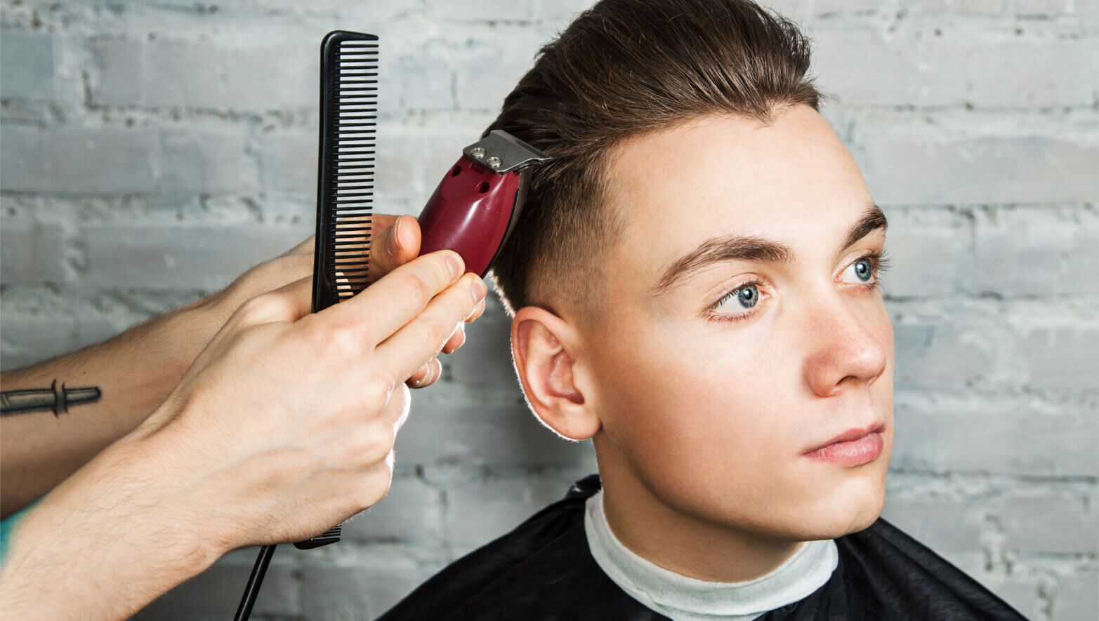 Barber hair styling of young guy in the barbershop on brick wall background, hairdresser makes hairstyle for a young man. Pompadour hairstyle.