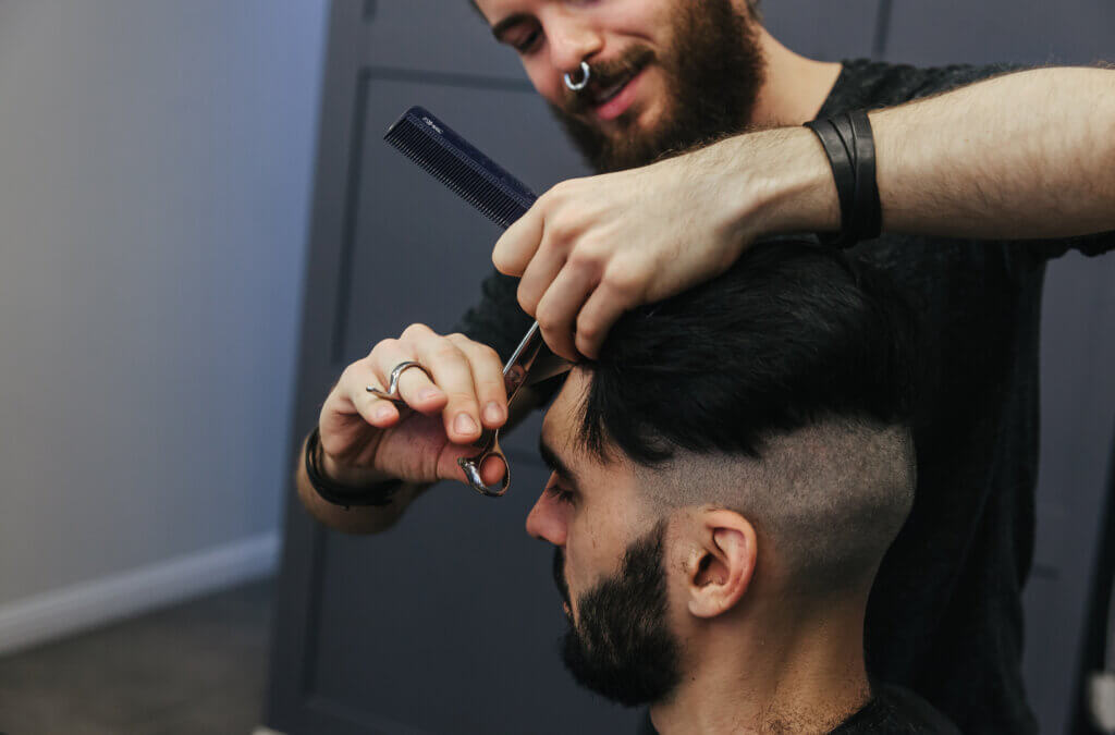 Male barber combing and shaving hair of a male client at barbershop